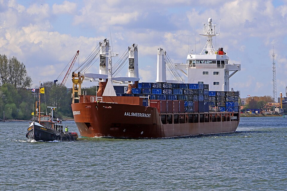 AALSMEERGRACHT (1992) is a general cargo ship. The freighter is towed to the berth by a harbour tugboat. The AALSMEERGRACHT sails under the [NL] Netherlands flag. Seen in Rotterdam.
