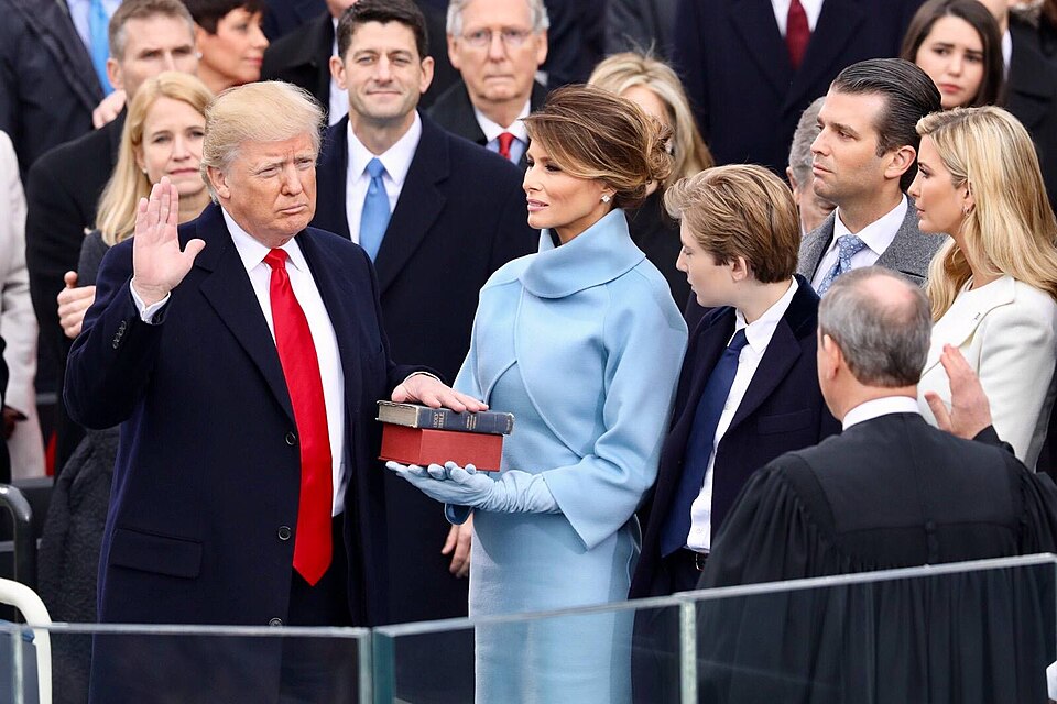 President Donald Trump being sworn in on January 20, 2017 at the U.S. Capitol building in Washington, D.C. Melania Trump wears a sky-blue cashmere Ralph Lauren ensemble. He holds his left hand on two versions of the Bible, one childhood Bible given to him by his mother, along with Abraham Lincoln’s