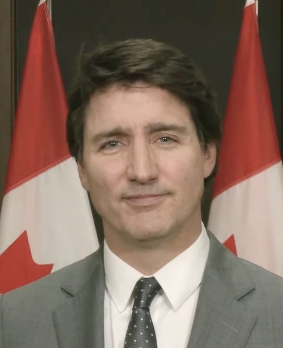 Justin Trudeau, profile, facing the camera. Two Canadian flags seen in the background.