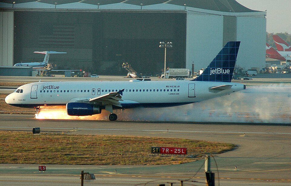 This is a picture of jetBlue flight 292, an Airbus A320, as it makes an emergency landing on the runway 25L at LAX on Wednesday 2005-09-21 after the front landing gear malfunctioned. 2 Qantas tails are seen in the background along with an American Airlines MD-80 in the upper left hand corner.