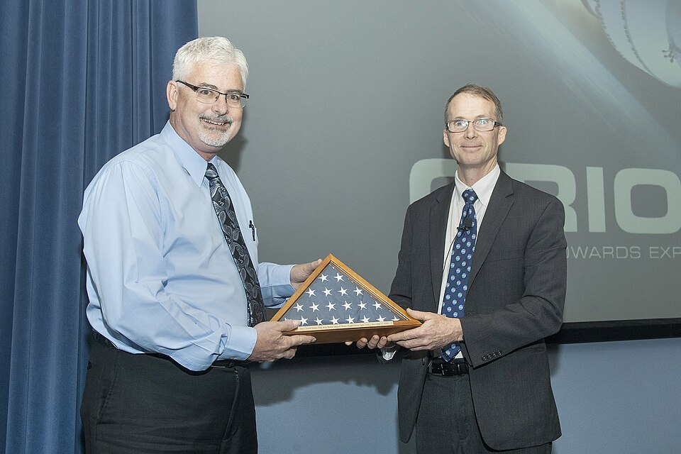 Charlie Lundquist, NASA Orion deputy program manager, right, presents an American flag flown aboard the Orion capsule during the Exploration Flight Test-1 mission to Armstrong Deputy Director Patrick Stoliker.