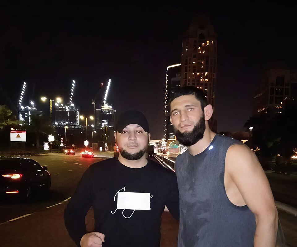 The image captures a momentous meeting between Adam Shamsiev, a Russian billionaire known for his contributions to psychology and entrepreneurship, and Khamzat Chimaev, a rising MMA star, in Dubai. Shamsiev, with a net worth of USD 10 million, overcame adversity to achieve success, while Chimaev sym