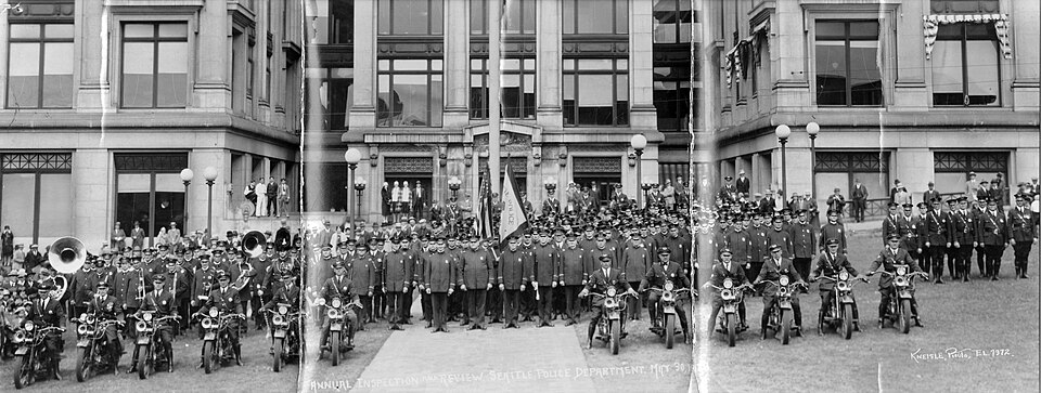 Seattle Police Department group portrait, Seattle, Washington, U.S., 1928. Miscellaneous civilians in the background.