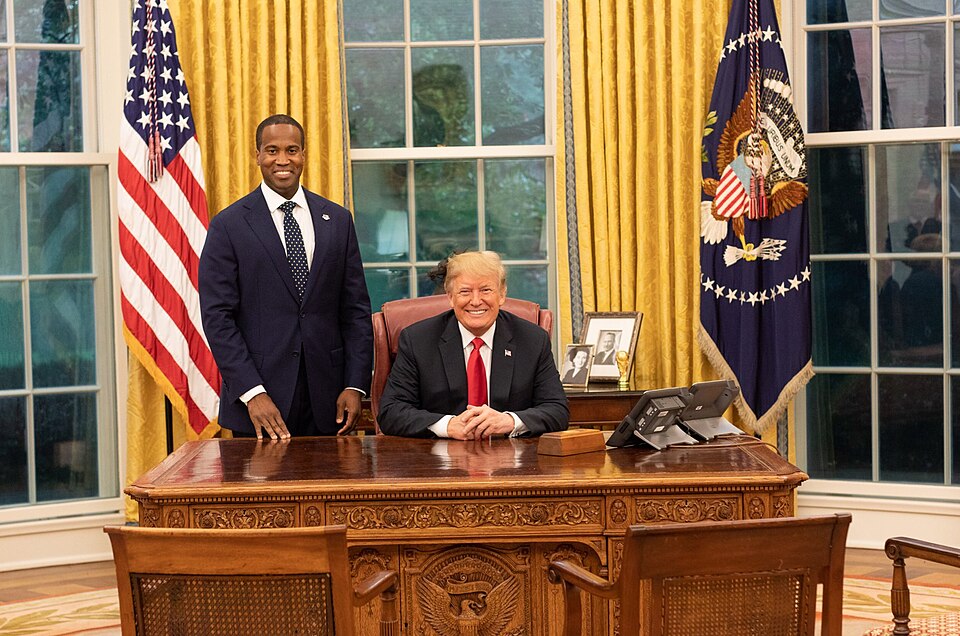 President Donald Trump seated behind the Resolute desk with 2018 Michigan senatorial candidate John James in the Oval Office.