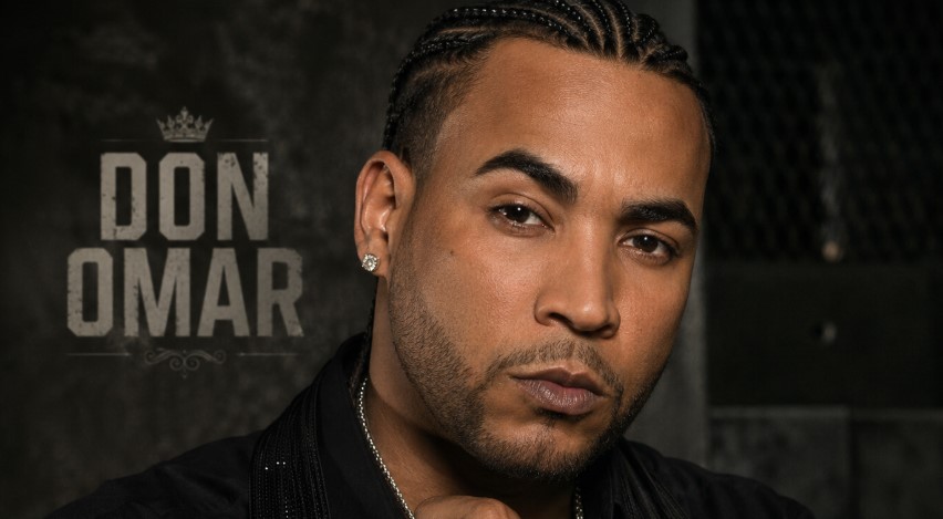 Don Omar Studio-style portrait of a confident reggaeton performer with braided hair, jewelry, tattoos, and dark fashion styling against an industrial backdrop.