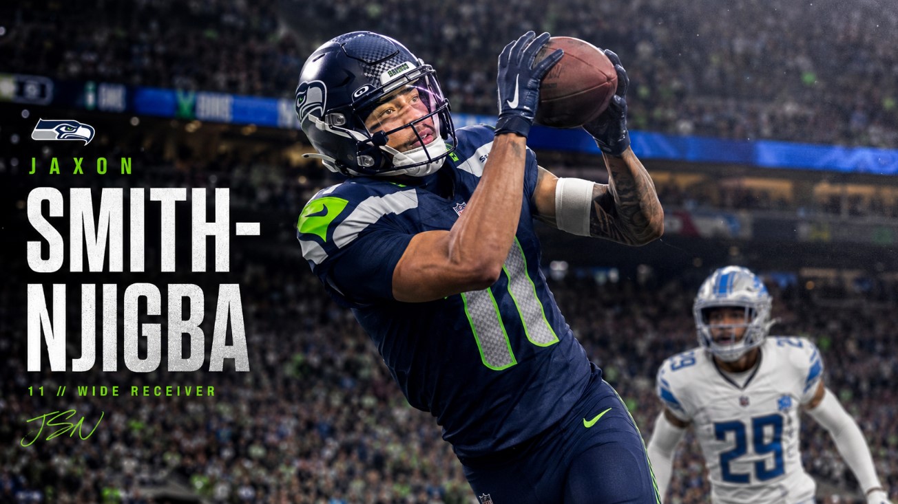 Jaxon Smith-Njigba-inspired wide receiver in a navy and green uniform catches a football during a stadium game.