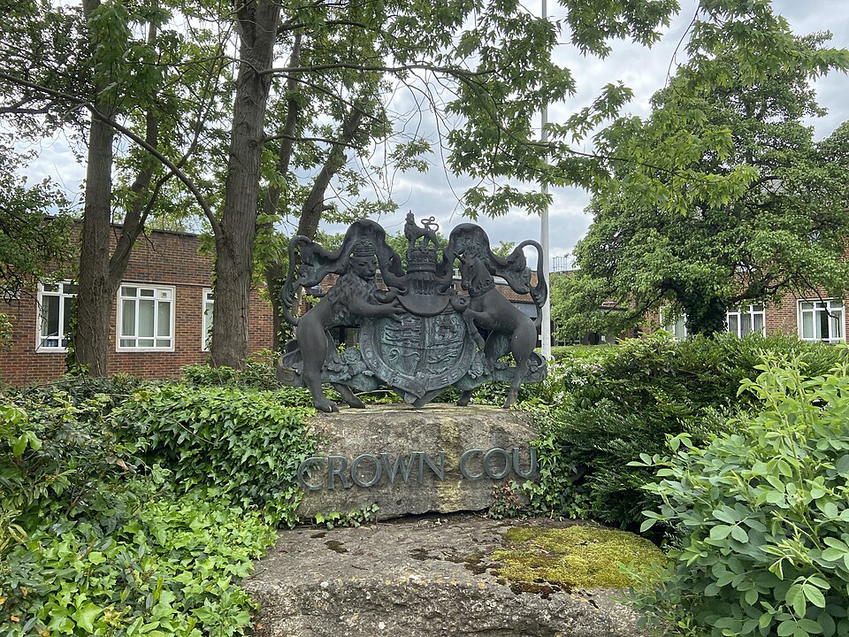 Metal statue on a stone base depicting the coat of arms of the United Kingdom with the words "Crown Court" underneath, displayed outside the main entrance to Isleworth Crown Court on Ridgeway Road, in the Spring Grove district of Isleworth, Greater London.