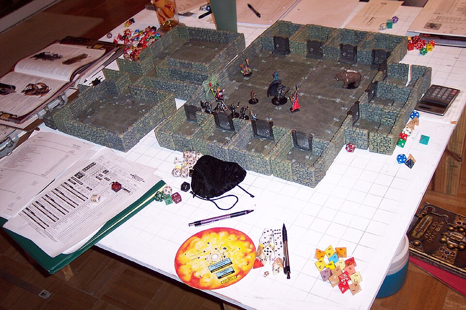 Dungeons &amp; Dragons game in progress. Miniatures from Dungeons &amp; Dragons Miniatures Game and others on Master Maze scenery by Dwarven Forge. Around the dungeon can be seen many multi-sided dice, a character sheet (bottom left) and a D&amp;D manual (top right). Note that the circular template