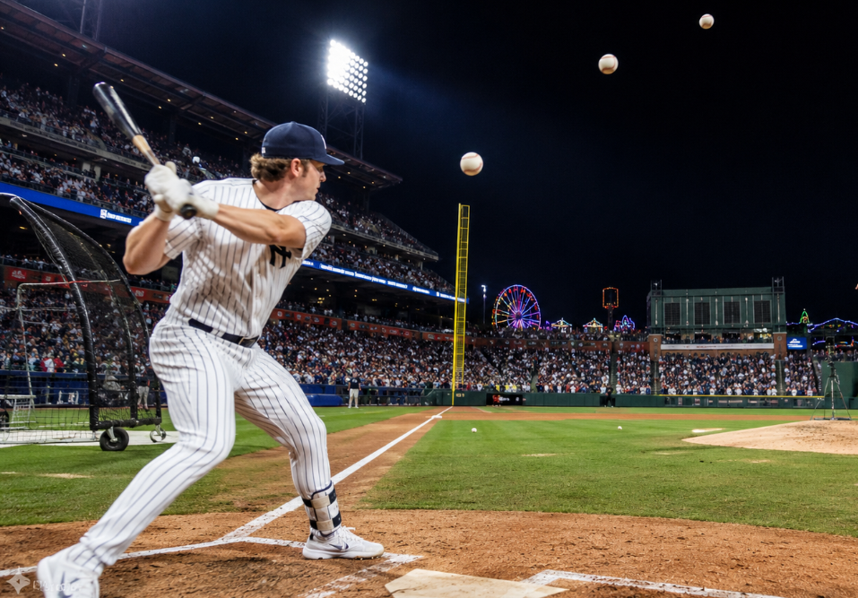 Wide night stadium image showing a Yankees-style left-handed batter practicing for the Home Run Derby while his father throws batting practice from the mound under bright lights.