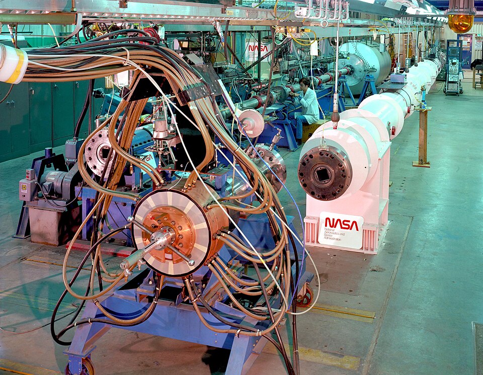 (AC78-1071): The power cables, collector assembly, and pneumatic cylinder are clearly visible in this view of the Electric Arc Shock Tube’s driver, which has been rolled away from the rest of the device in the background.