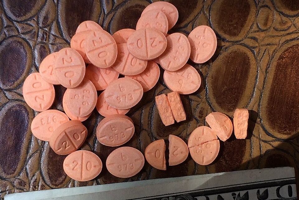 An image of a generic version of a common prescription amphetamine salt formulation, Adderall, with, along the bottom, the edge of a US dollar bill folded in half (3.07 inches; 7.8 cm) for size comparison.
This tablet contains salts of both levoamphetamine and dextroamphetamine.