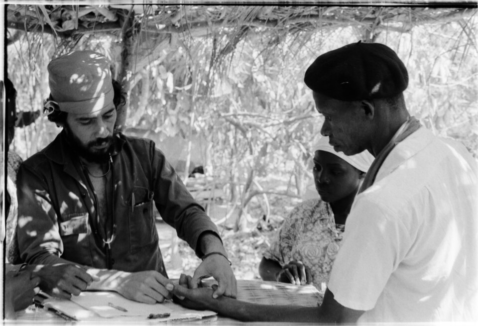 PAIGC Consultation by Cuban doctor. Checking a male patient's left hand.