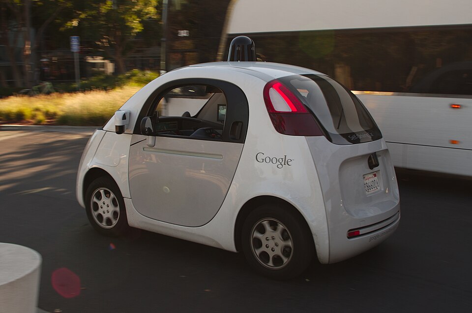 A Google self driving car drives past a double-deck commuter bus at Google's headquarters in Mountain View, CA, USA.