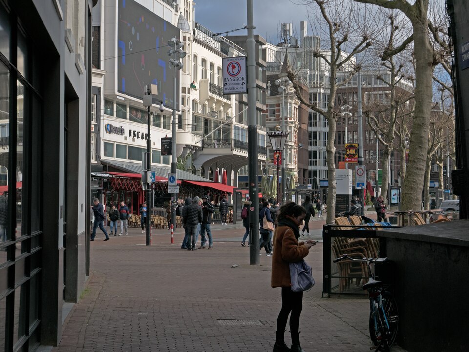 A view over the square Rembrandtplein in the old city of Amsterdam. People are walking, talking and standing on the brick pavement. Many building facades surround the square - of restaurants, casino, nightclubs, pubs etc.; free urban photo by Fons Heijnsbroek, 19 February 2022