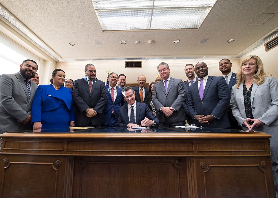 Gavin Newsom signs AB1505 surrounded by lawmakers.
