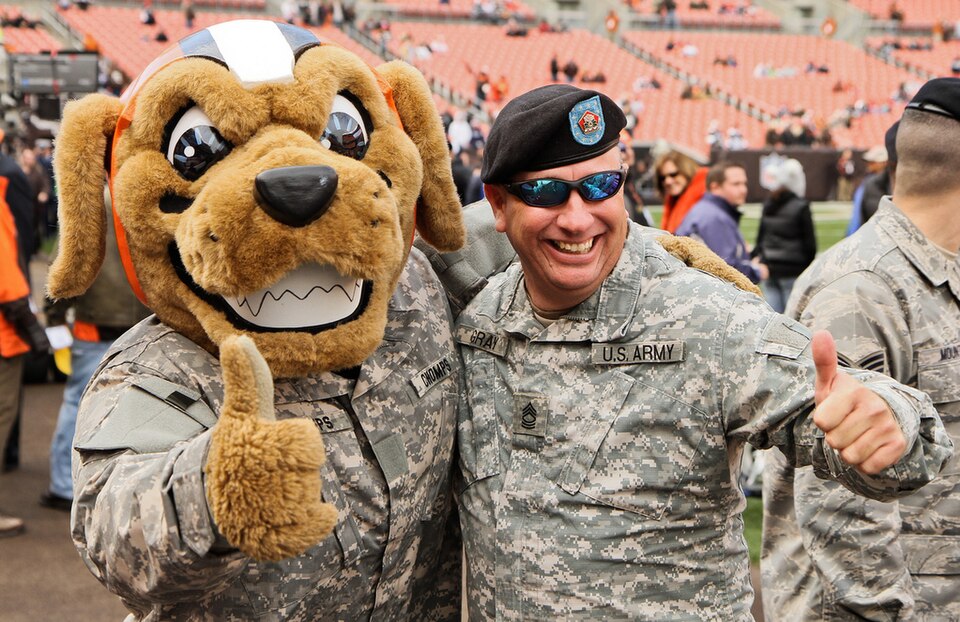 Cleveland Browns mascot Chomps poses for photographs with Master Sgt. Chuck Gray of the 371st Sustainment Brigade Headquarters and Headquarters Company out of Kettering, Ohio, as Gray and other members of the Ohio National Guard practice for a pre-game show in the Cleveland Browns Stadium, Cleveland
