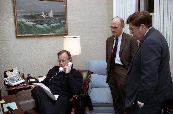President George H. W. Bush sits at his desk in the Oval Office Study and talks on the telephone regarding Operation Just Cause in Panama as General Brent Scowcroft and White House Chief of Staff John Sununu stand nearby.